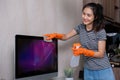 A beautiful housewife wears orange gloves and uses a cloth to clean the desktop computer screen in the living room. Royalty Free Stock Photo