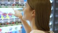 Beautiful hungry woman picking item out of vending machine in mall. Choosing unhealthy snacks being hungry