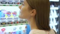 Beautiful hungry woman picking item out of vending machine in mall. Choosing unhealthy snacks being hungry