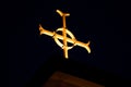 Beautiful illuminated golden cross atop a church at night time with darkened sky in background