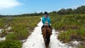 image of a person riding a horse along a white sand path in the middle of a rural nature landscape