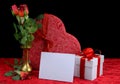 Beautiful image in shades of red for Valentine`s Day in February. Silk roses in brass vase with gift and blank card on velvety tab