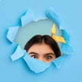 Beautiful Indian teenage girl peeping through hole in ripped blue paper, having amazed or shocked face expression Royalty Free Stock Photo