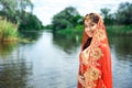 Beautiful Indian woman wearing traditional red dress posing against river