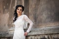Beautiful innocent brunette bride in white dress posing near church wall Royalty Free Stock Photo