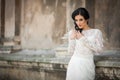 Beautiful innocent brunette bride in white dress posing near church wall Royalty Free Stock Photo