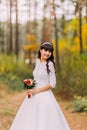 Beautiful innocent young brunette bride in classic white dress stands on forest trail