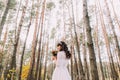 Beautiful innocent young brunette bride in gorgeous white dress with bouquet at pine wood forest Royalty Free Stock Photo