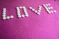 Beautiful inscription love made from white round smooth medical pills, vitamins, antibiotics and copy space on a bright purple Royalty Free Stock Photo