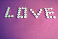 Beautiful inscription love made from white round smooth medical pills, vitamins, antibiotics and copy space on a bright purple Royalty Free Stock Photo