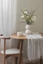 The beautiful interior of the living room - round wooden table with a muslin tablecloth, a vase with a bouquet of flowers and a Royalty Free Stock Photo