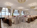 Beautiful interior of the restaurant in a modern hotel with white cloth tables and soft chairs, serving tables with live roses Royalty Free Stock Photo