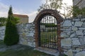 Beautiful iron gate with patterns in a stone wall with a brick arch. A church with a tiled roof is visible. Blue sky Royalty Free Stock Photo