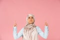 Islamic woman in hijab pointing up, isolated on pink