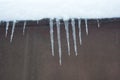 Winter snowy day, icicles from the roof of a metal garage of brown color with fluffy white snow