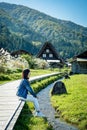 Beautiful Japanese girl with a background of Shirakawago village during autumn with a triangle house, rice field, and pine mountai Royalty Free Stock Photo