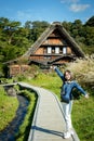 Beautiful Japanese girl with a background of Shirakawago village during autumn with a triangle house, rice field, and pine mountai