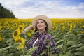 Beautiful joyful and smiling middle-aged farmer woman in a straw hat and shirt stands in a harvest field of sunflowers on a sunny Royalty Free Stock Photo