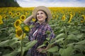 Beautiful joyful and smiling middle-aged farmer woman in a straw hat and shirt stands in a harvest field of sunflowers on a sunny Royalty Free Stock Photo