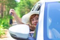 A beautiful joyful woman looks out of the car window with a key in her hand on a summer sunny day against the backdrop of green tr Royalty Free Stock Photo