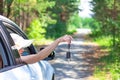 Beautiful joyful woman looks out of the car window with a key in her hand on a summer sunny day against the backdrop of green tree Royalty Free Stock Photo