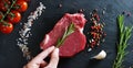 Beautiful juicy fresh meat steak on a table with salt, rosemary, garlic, and tomato on a black background, top view. Concept: fres