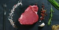 Beautiful juicy fresh meat steak on a table with salt, rosemary, garlic, and tomato on a black background, top view. Concept: fres