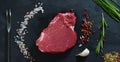Beautiful juicy fresh meat steak on a table with salt, rosemary, garlic, and tomato on a black background, top view. Concept: fres