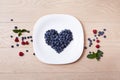 Beautiful juicy ripe natural organic raspberries blackberries blueberries and mint blue tablecloth dots white dish heart shape Royalty Free Stock Photo
