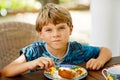 Beautiful kid boy eating apple pie in restaurant on vacations. Happy healthy child in an outdoor cafe in summer time Royalty Free Stock Photo