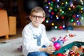 Beautiful kid boy with eye glasses and colorful vintage xmas toys and balls in old suitcase. Child decorating Christmas Royalty Free Stock Photo