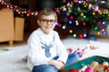 Beautiful kid boy with eye glasses and colorful vintage xmas toys and balls in old suitcase. Child decorating Christmas Royalty Free Stock Photo