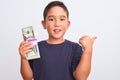 Beautiful kid boy holding dollars standing over isolated white background pointing and showing with thumb up to the side with Royalty Free Stock Photo