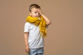 Beautiful kid boy wearing casual t-shirt and yellow scarf standing over isolated light background Touching forehead for