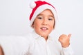 Beautiful kid boy wearing Christmas Santa hat make selfie over isolated white background pointing and showing with thumb up to the Royalty Free Stock Photo