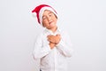 Beautiful kid boy wearing Christmas Santa hat standing over isolated white background smiling with hands on chest with closed eyes Royalty Free Stock Photo