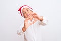 Beautiful kid boy wearing Christmas Santa hat standing over isolated white background smiling in love doing heart symbol shape Royalty Free Stock Photo