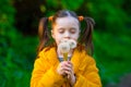 Beautiful kid girl with ponytails in a yellow jacket holds white fluffy dandelions and smiles Royalty Free Stock Photo