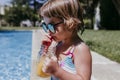 Beautiful kid girl at the pool drinking healthy orange juice and having fun outdoors. Summertime and lifestyle concept Royalty Free Stock Photo