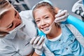 Beautiful kid girl smiling in dentist`s chair the office treats teeth. Doctor mask and child looks at camera Royalty Free Stock Photo