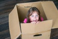 Beautiful kid sits in a mail box. A little girl is in a cardboard box. Baby moves to a new apartment. The child plays funny.