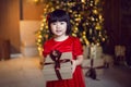 beautiful Korean child girl in red dress stands at the Christmas tree on Christmas day Royalty Free Stock Photo