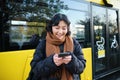 Beautiful korean girl, student on bus stop, looking at her smartphone, checking timetable, reading text message, wearing Royalty Free Stock Photo