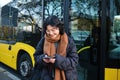 Beautiful korean girl, student on bus stop, looking at her smartphone, checking timetable, reading text message, wearing Royalty Free Stock Photo