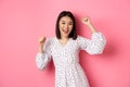 Beautiful korean woman dancing and having fun, smiling happy at camera, posing against pink background Royalty Free Stock Photo