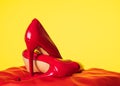 Lacquered shiny women`s red stilettos lie on a pillow on a yellow background
