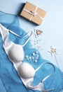 A beautiful lacy white bra lies on a blue fabric, next to it are pearl stars, a herringbone and a gift box. Royalty Free Stock Photo