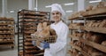 Beautiful lady baker in a white uniform holding a basket with fresh bread and smiling cute in front of the camera
