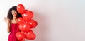 Beautiful lady with curly hair, standing near valentines holiday balloons and waving hand, saying hello, standing