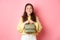 Beautiful lady holding her purse in hands near chest, smiling and looking excited at camera, waiting for something with Royalty Free Stock Photo
